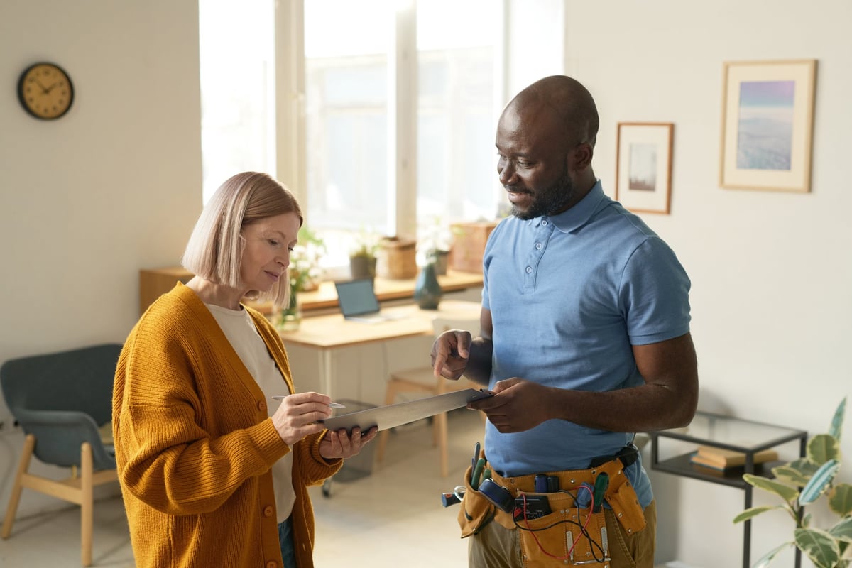 Side view portrait of smiling African American man handing clipboard to female client signing contract for home repairs services