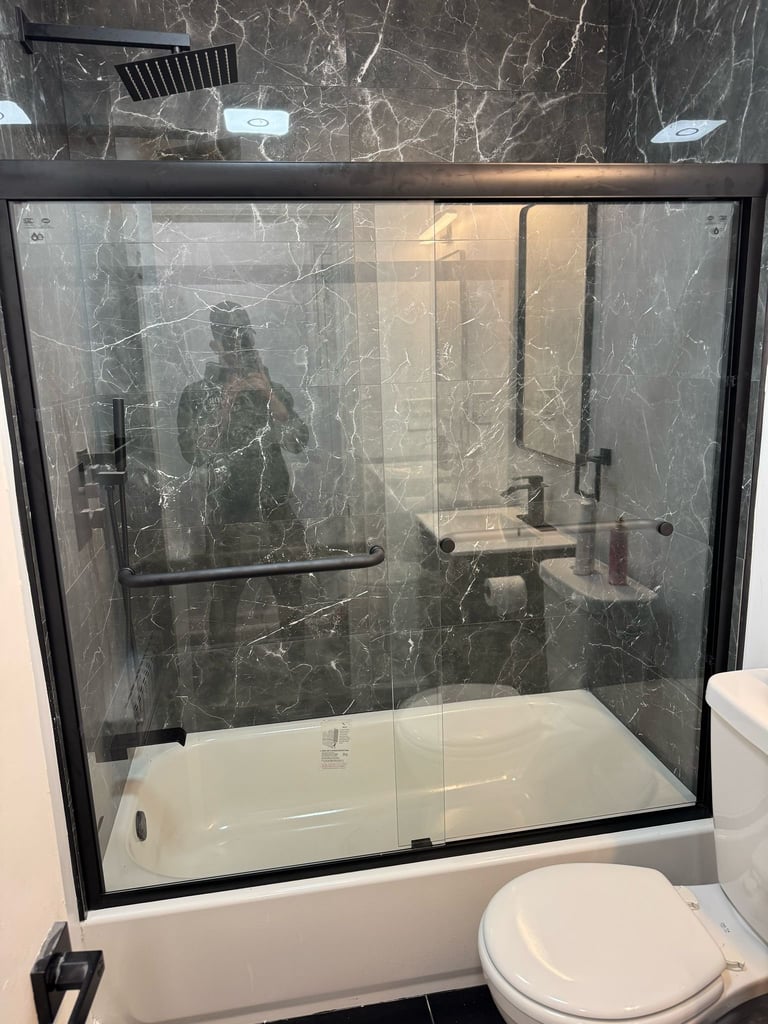 Modern bathroom shower enclosure with black frame and dark marble tile walls, white base, and white toilet visible beside it