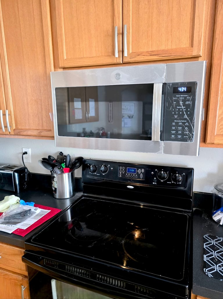 Kitchen counter with stainless steel microwave above black electric range and wooden cabinets