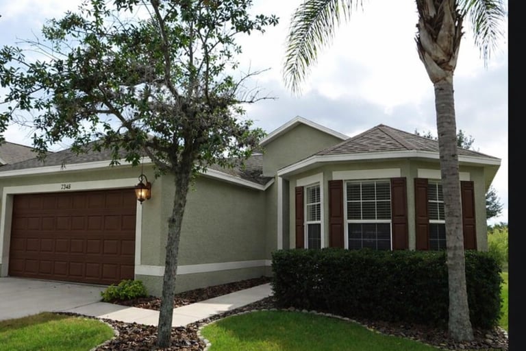Single-story cream and brick house with brown garage door, palm tree, and landscaped front yard